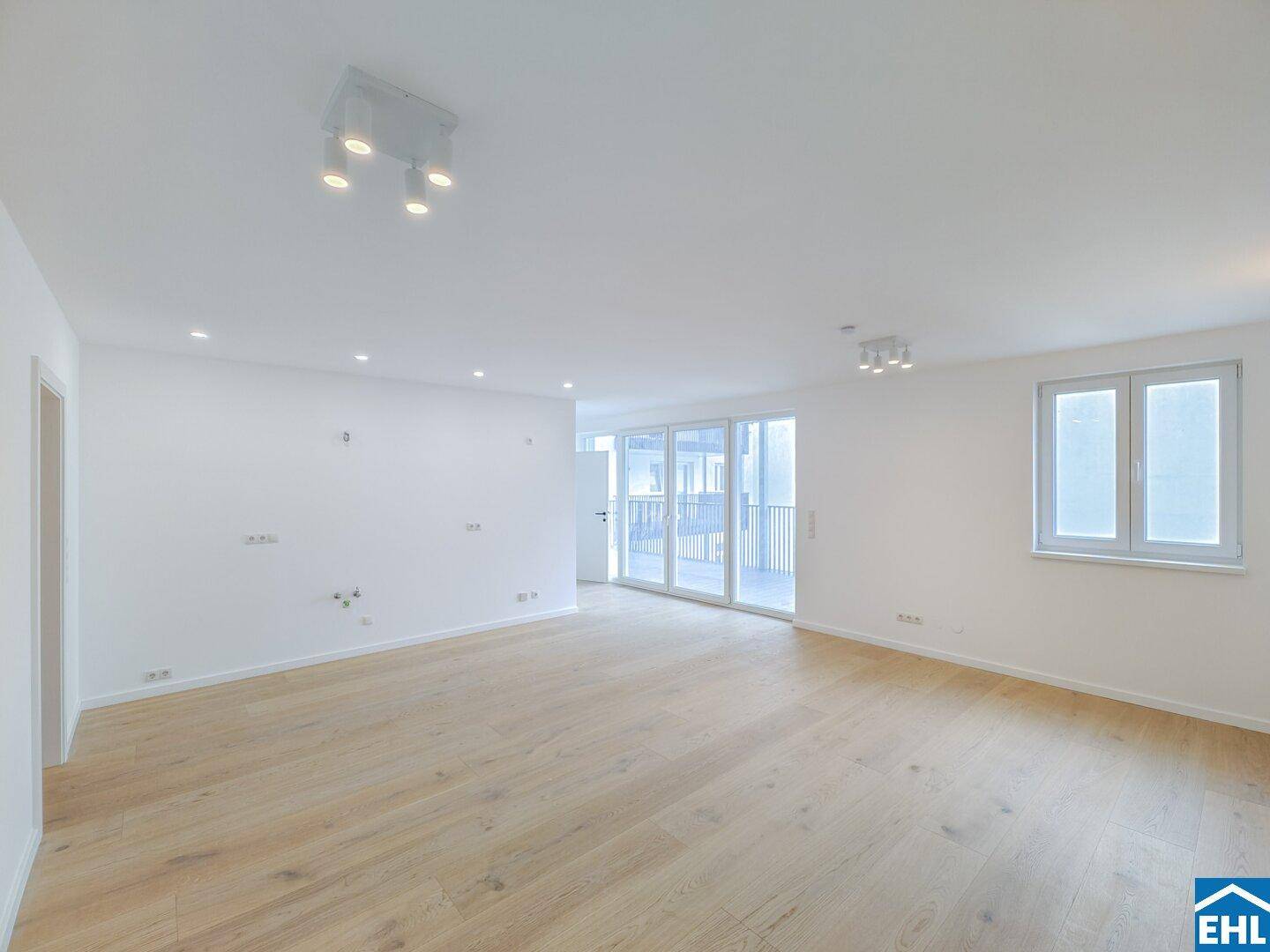 Großzügiger Wohnraum mit hellem Dielenboden und breiter Glasfront zum Balkon.