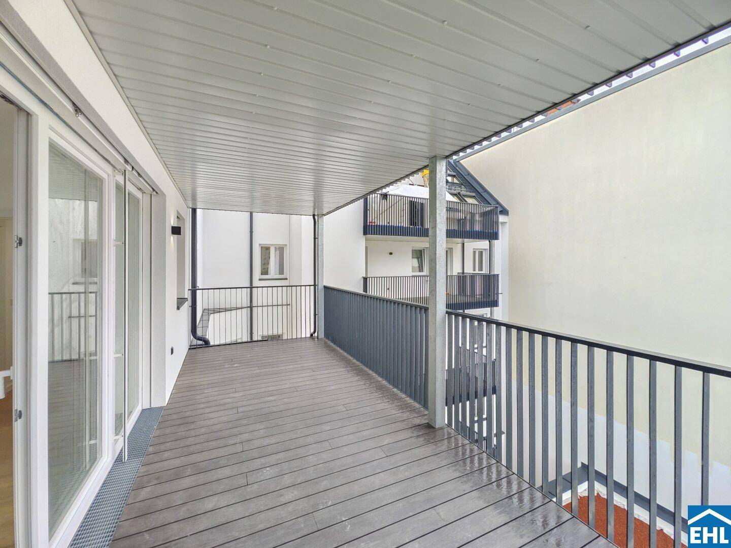 Überdachter Balkon mit Holzboden und Blick auf den Innenhof, ideal für entspannte Stunden.