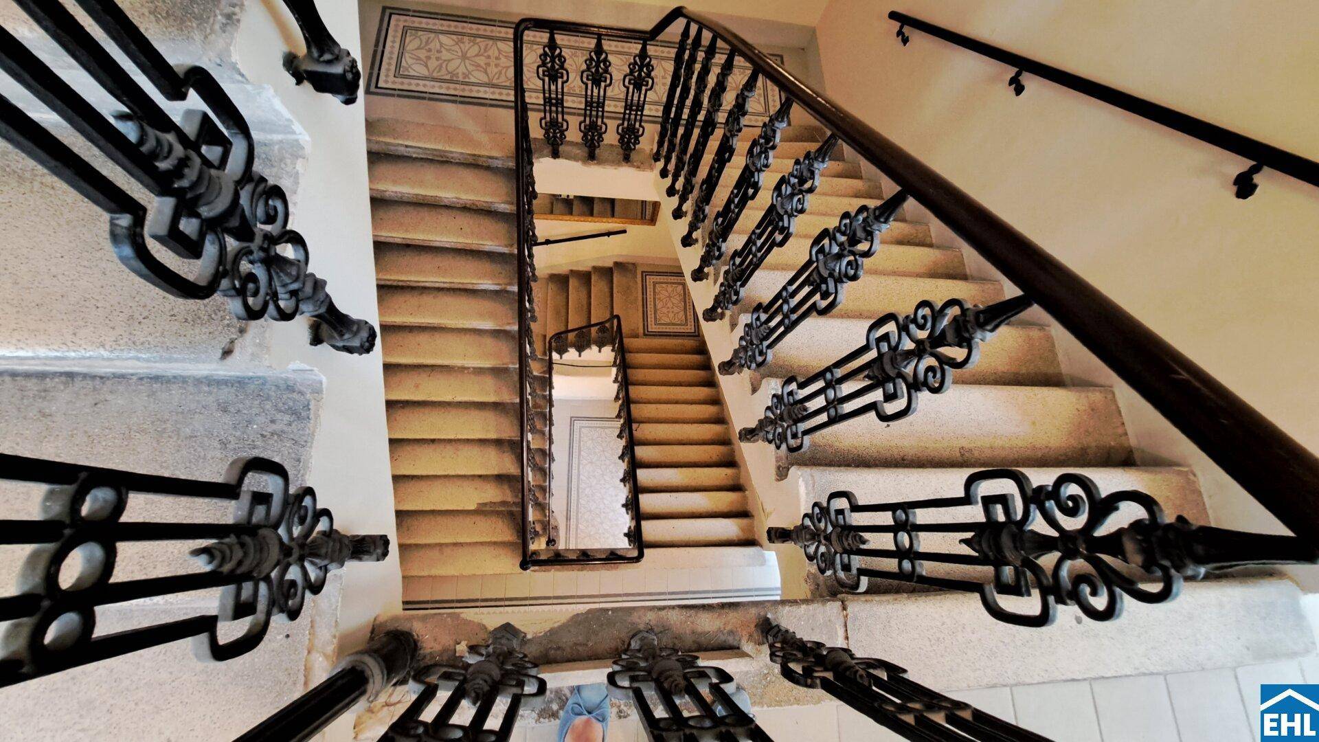 Historisches Treppenhaus mit kunstvollem schmiedeeisernem Geländer und Steinstufen in einem Altbau.