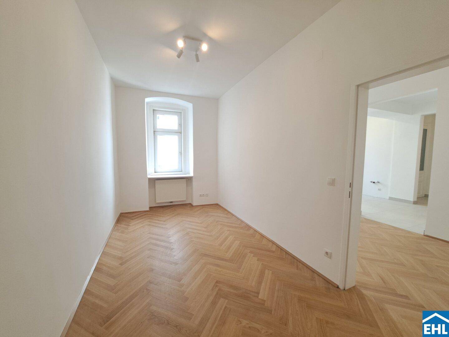 Geräumiges Zimmer mit hellem Fischgrätparkett und einem Fenster, das viel Tageslicht hereinlässt.