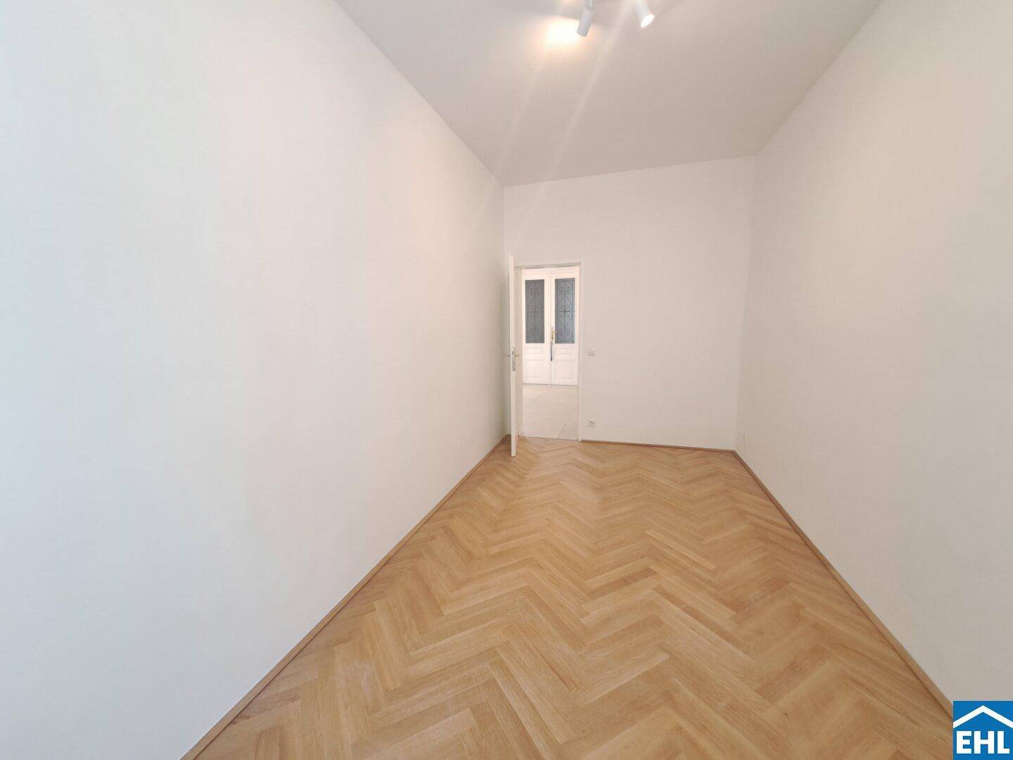 Geräumiges Zimmer mit Fischgrätparkett und einer klassischen Tür, die den Zugang ermöglicht.