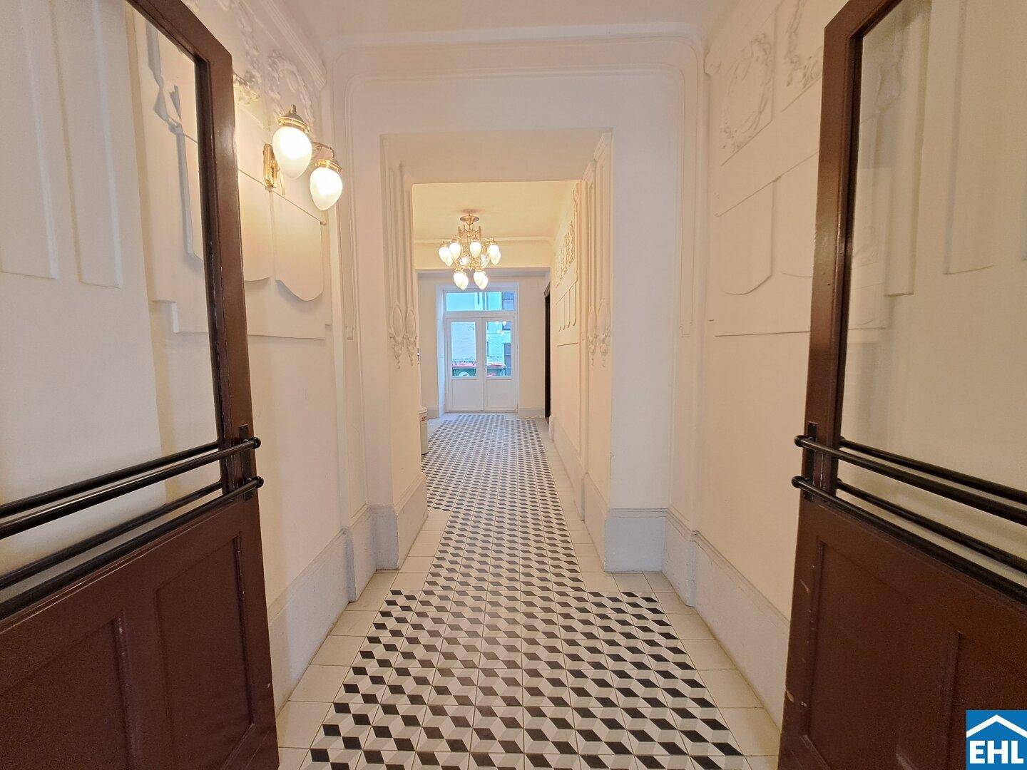 Eleganter Eingangsbereich mit gemustertem Fliesenboden, verzierten Türen und Stuck an der Decke.