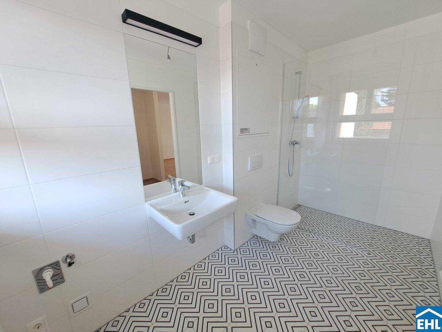 Modernes Badezimmer mit weißen Fliesen, stilvollem geometrischem Bodenmuster und wandhängendem WC.