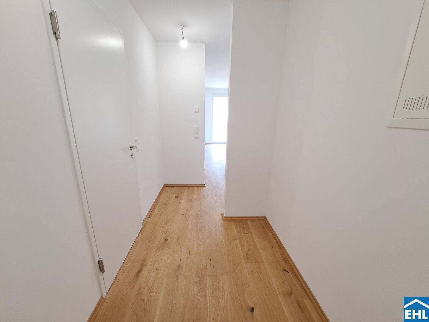 Heller Flur mit elegantem Holzparkett und weißen Wänden, der zu den weiteren Räumen führt.
