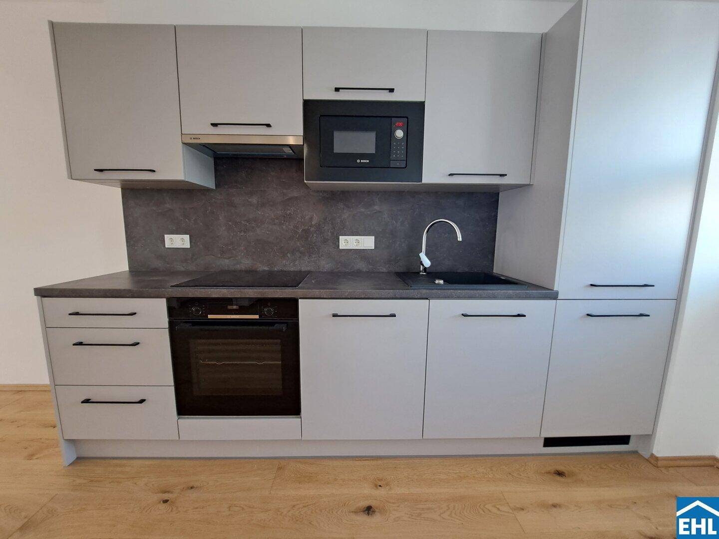 Moderne Einbauküche in Grau mit Induktionskochfeld, Backofen und Mikrowelle.