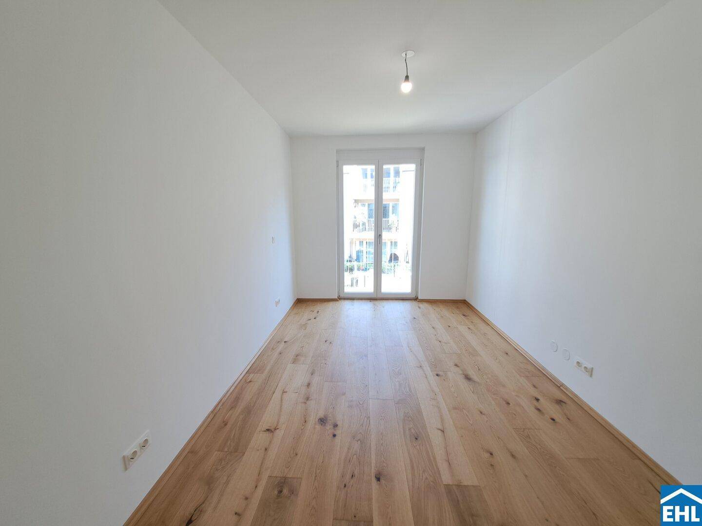 Helles Schlafzimmer mit Holzboden und Zugang zu einem Balkon.