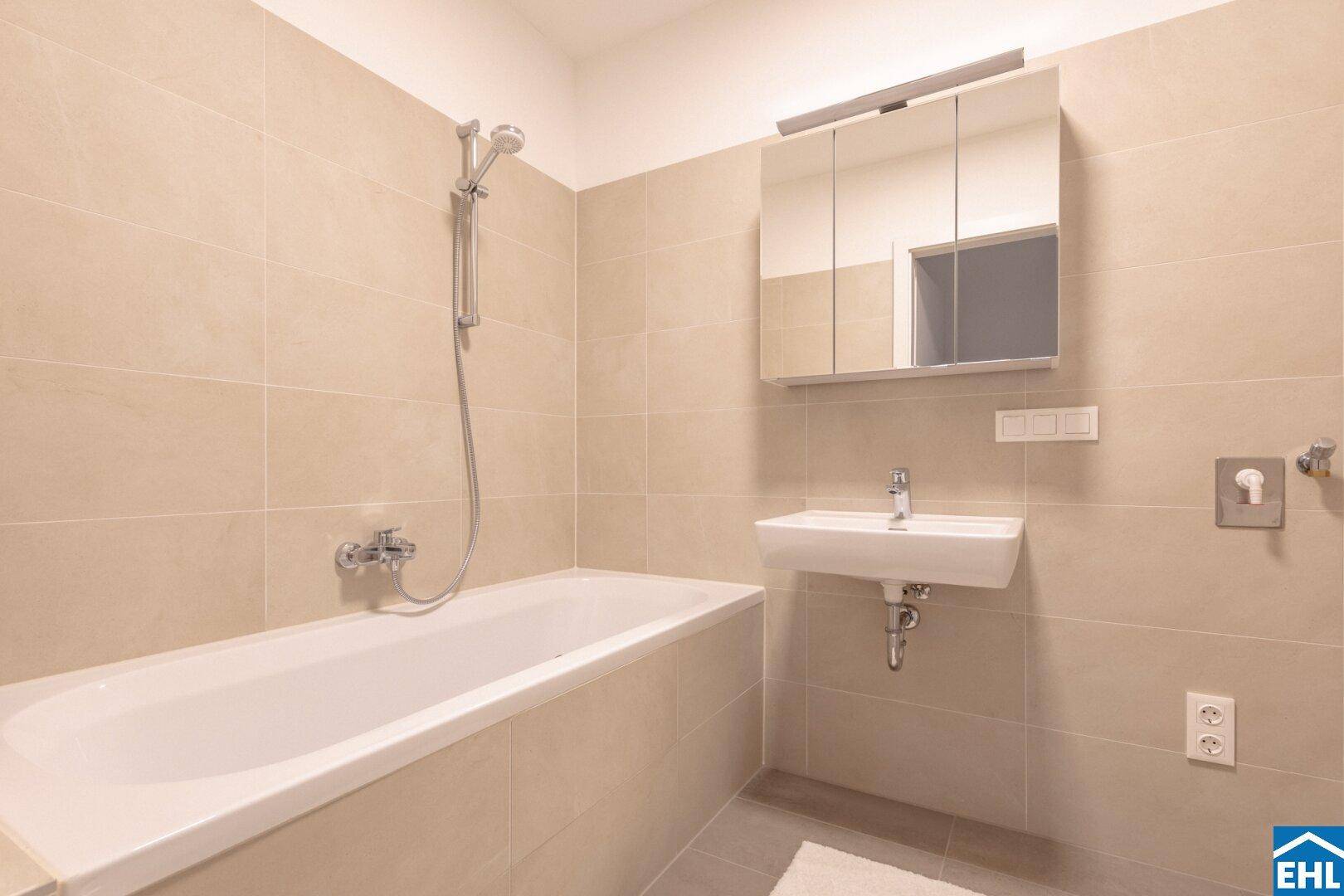 Modernes Badezimmer mit Badewanne, Waschbecken und Spiegelschrank, gefliest in hellen Beigetönen.