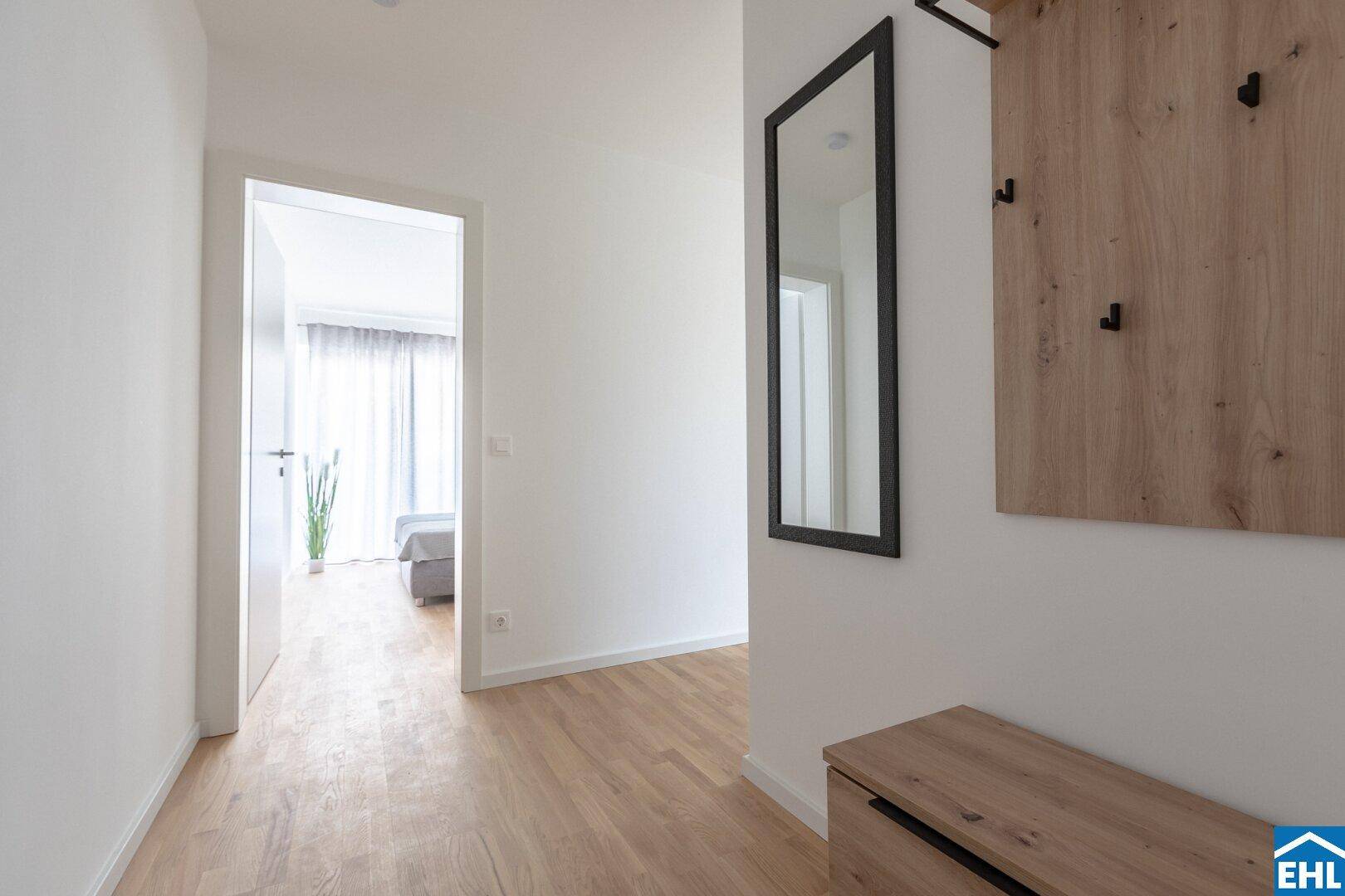 Heller Flur mit Garderobe, Spiegel und Holzboden, der zu den weiteren Räumen führt.