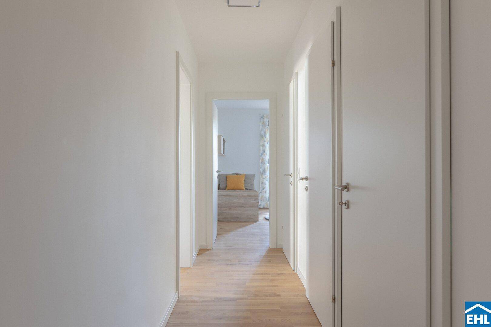 Langer, heller Flur mit Holzboden, der einen Blick in ein angrenzendes Schlafzimmer bietet.