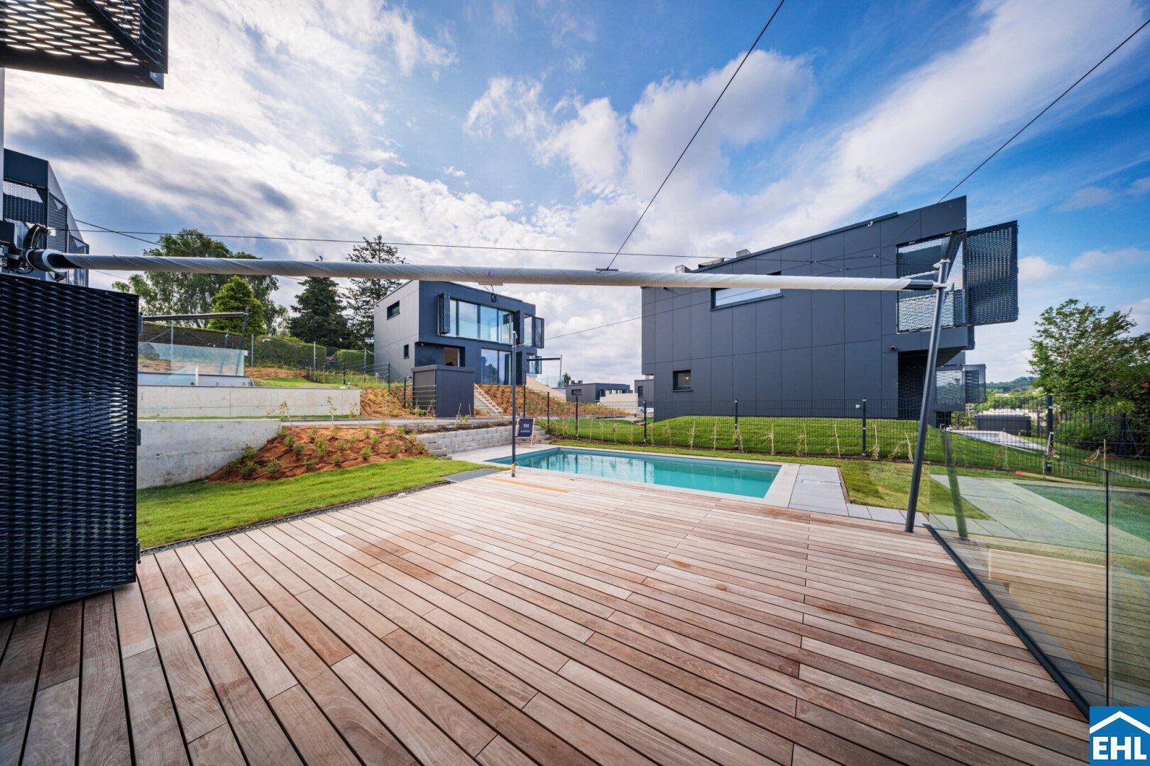 Geräumige Holzterrasse mit Blick auf den Pool und weitere moderne Gebäude in der Umgebung.