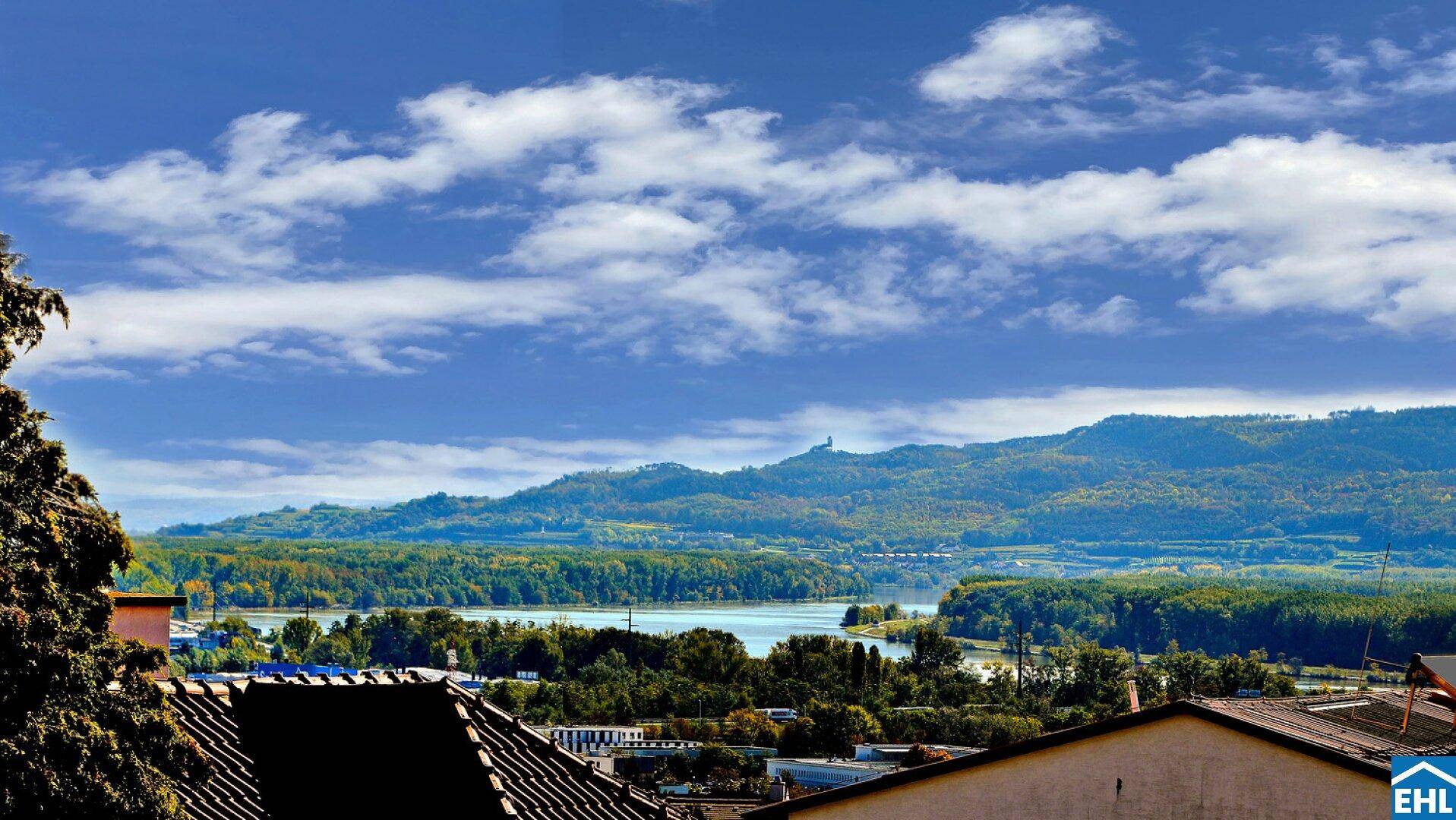 Weitläufiger Panoramablick über eine Seenlandschaft mit bewaldeten Hügeln und Bergen im Hintergrund.