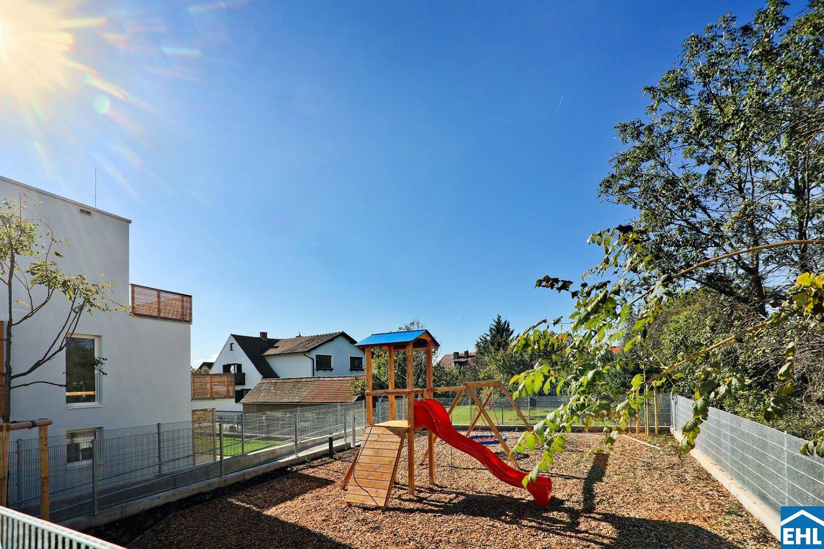 Kinderspielplatz mit Rutsche und Schaukeln, umgeben von einer sicheren Holzschnitzeloberfläche.