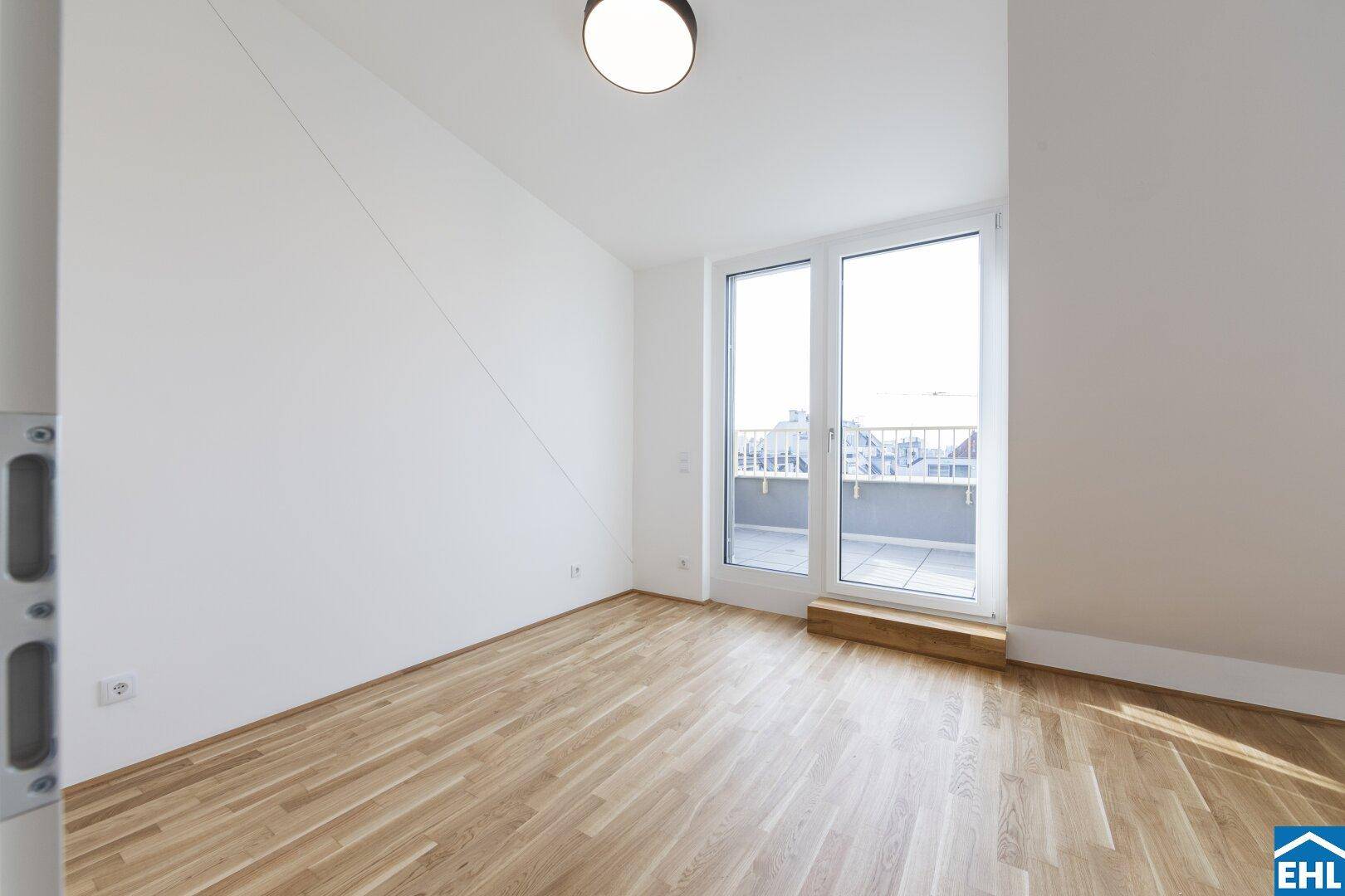 Helles Zimmer mit Parkettboden, weißen Wänden und großem Fenster mit Zugang zu einem Balkon.