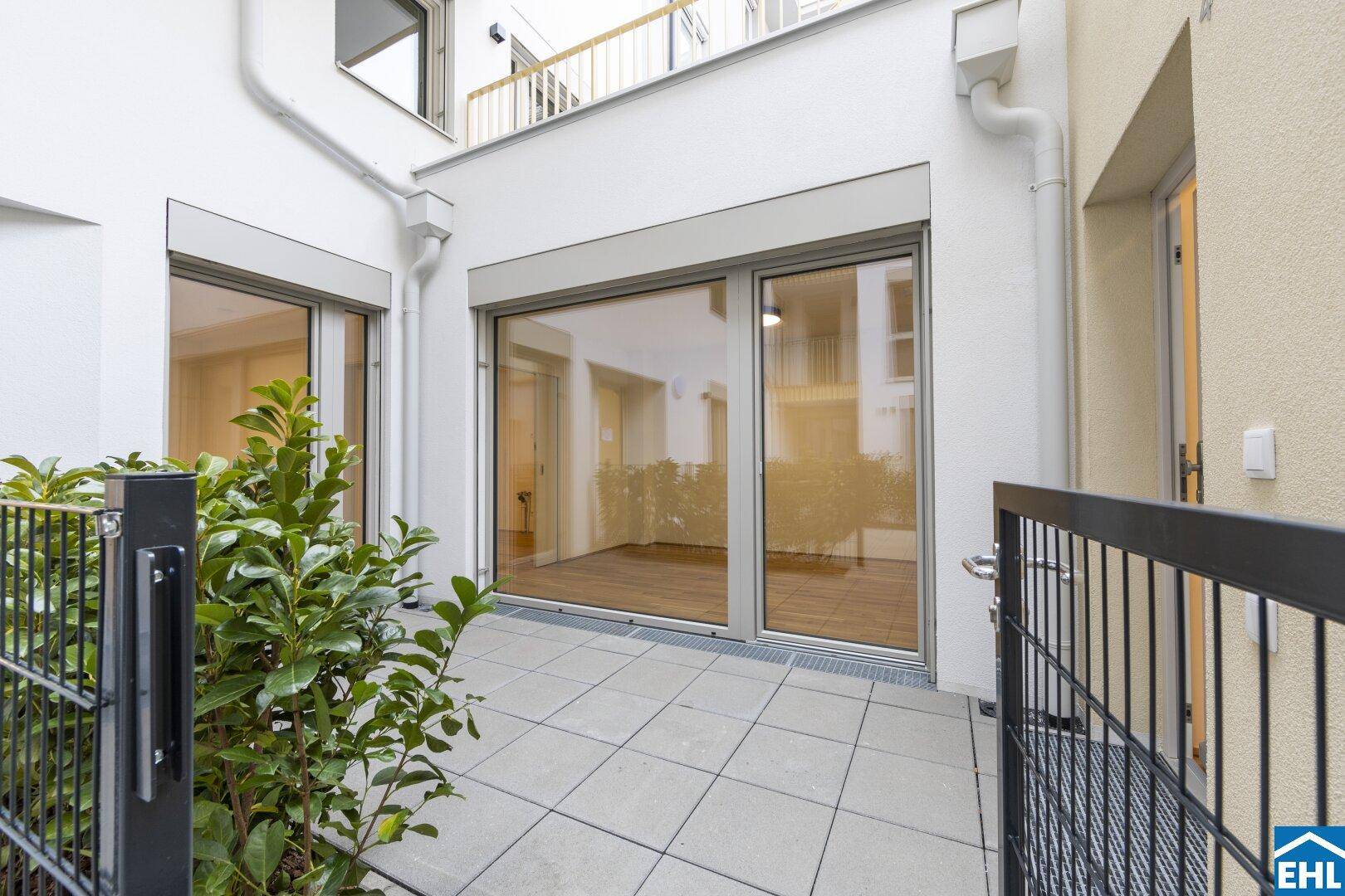 Private Terrasse mit Fliesenboden und kleiner Hecke, umgeben von modernen Gebäudefassaden.