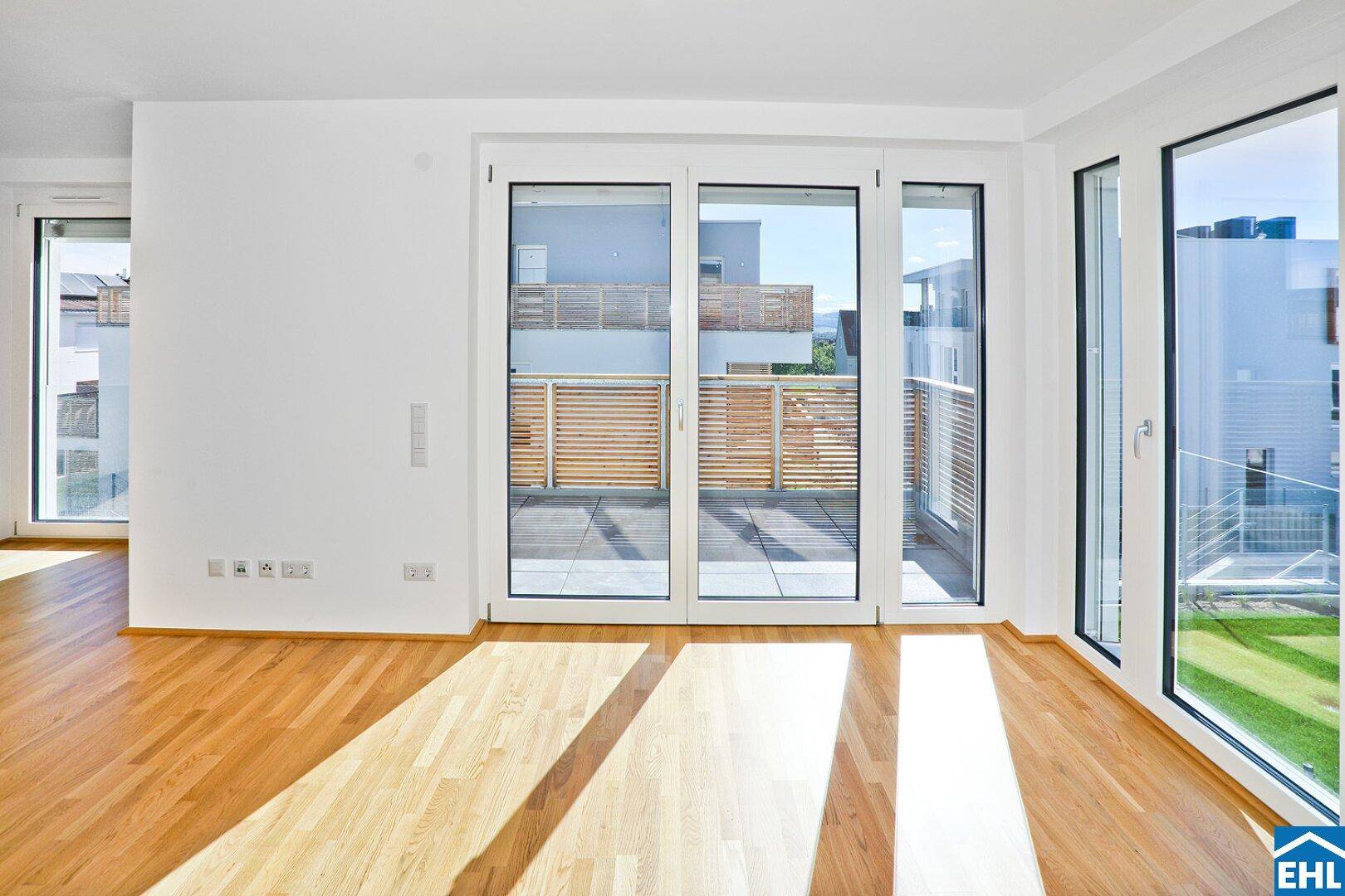 Lichtdurchfluteter Wohnbereich mit Holzboden und breitem Zugang zu einem Balkon.