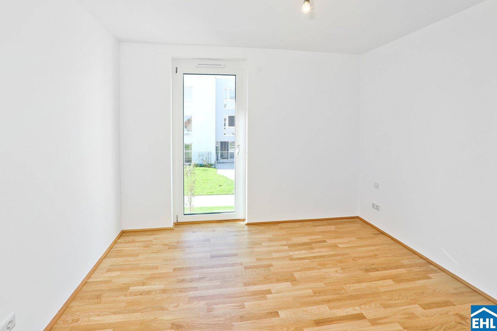 Helles Schlafzimmer mit Holzboden und Fenster mit Blick ins Grüne.