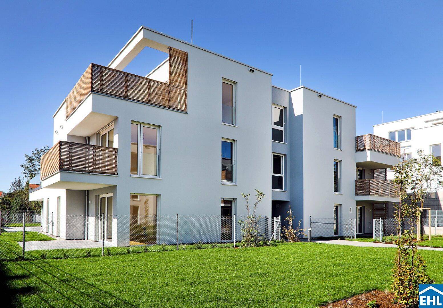 Zeitgenössisches Wohnhaus mit klaren Linien, Balkonen mit Holzgittern und sonnigen Rasenflächen.