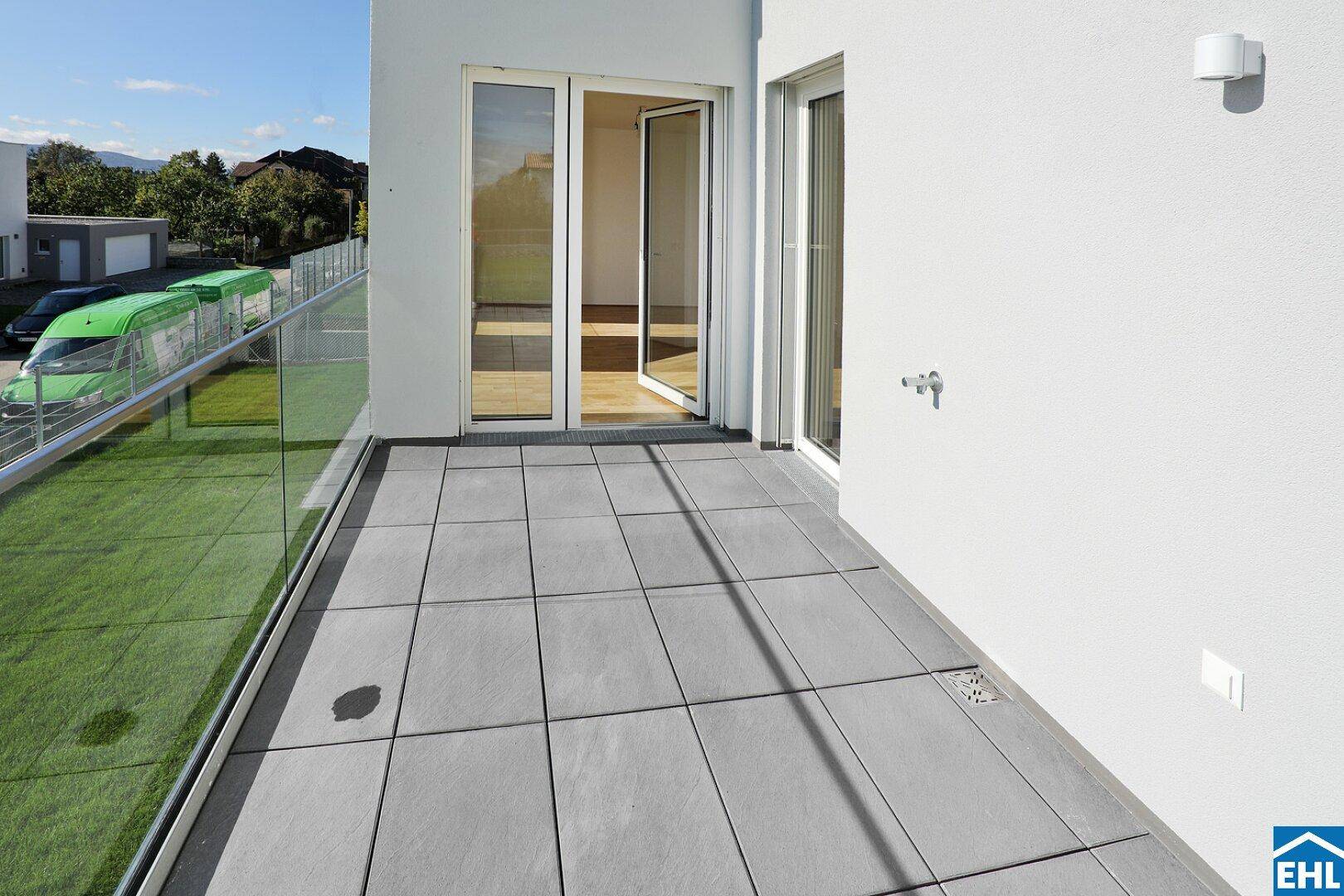 Helle Terrasse mit Zugang vom Innenbereich, ausgestattet mit modernen Fliesen und Glasgeländer.