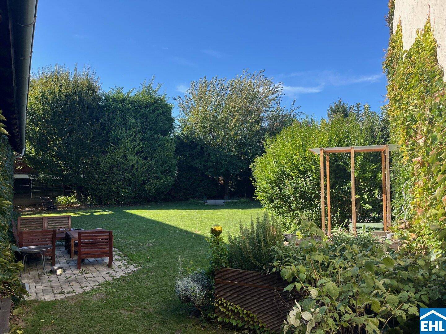Idyllischer Gartenbereich mit gepflasterter Terrasse, Holzmöbeln und üppiger Bepflanzung für entspannte Stunden.