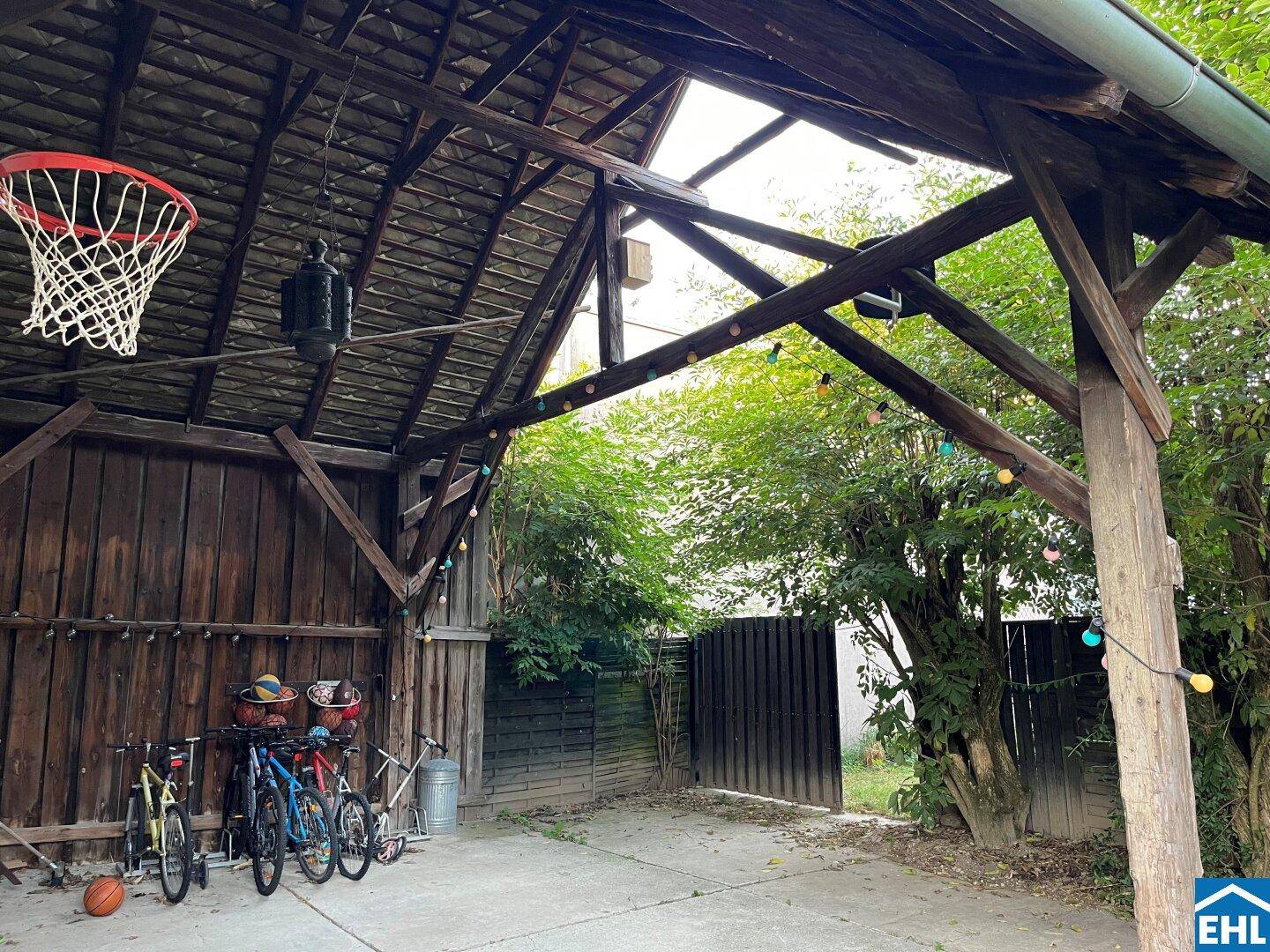 Offener Holzschuppen mit Basketballkorb, Fahrrädern und rustikalen Holzbalken, ideal für Freizeitaktivitäten.