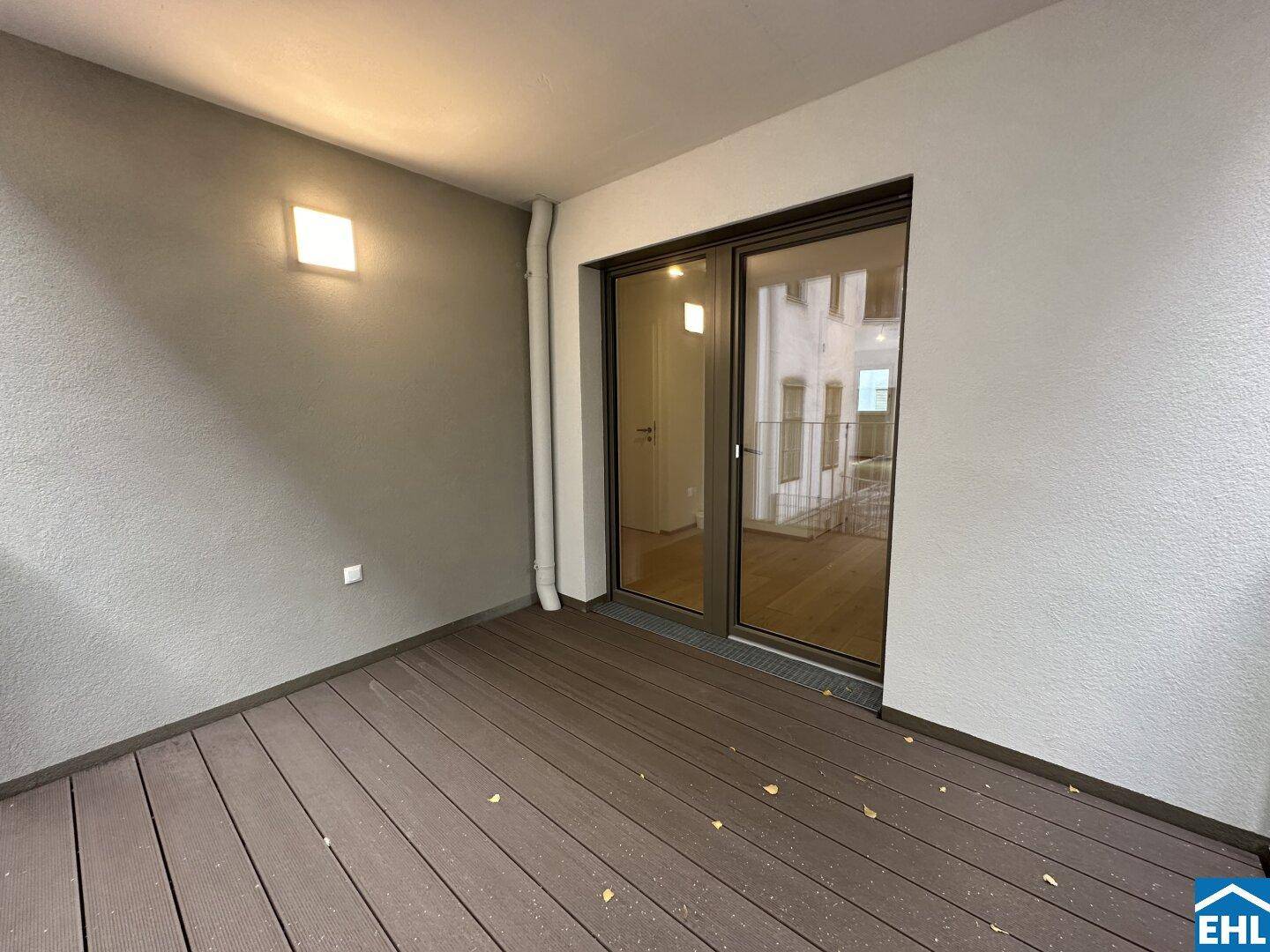 Heller Balkon mit Holzboden und großer Glasfront, die den Zugang zum Innenbereich ermöglicht.