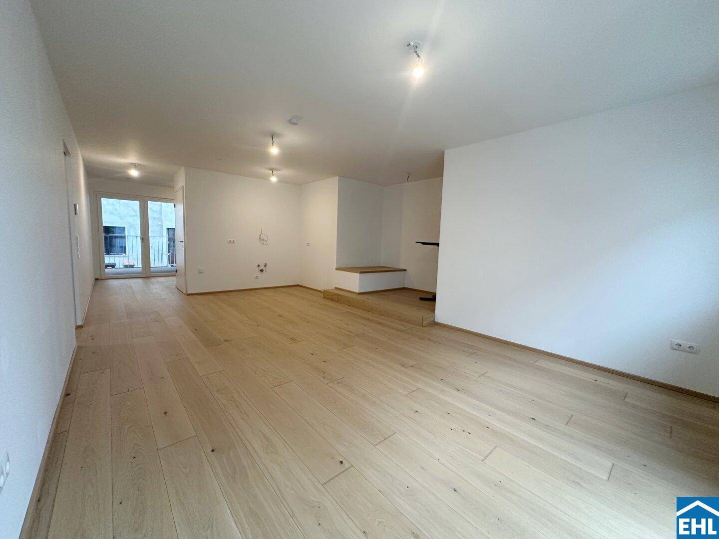 Geräumiger, heller Wohnbereich mit neuem Holzboden, weißen Wänden und Zugang zu einem Außenbereich.