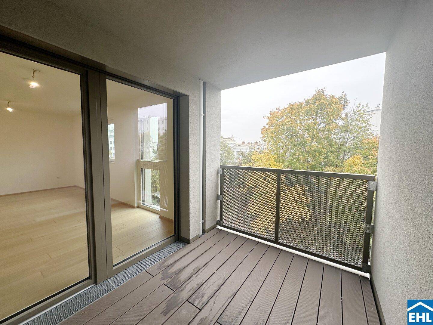 Moderner Balkon mit Holzdielen und einem Gittergeländer, bietet einen Blick auf Bäume.