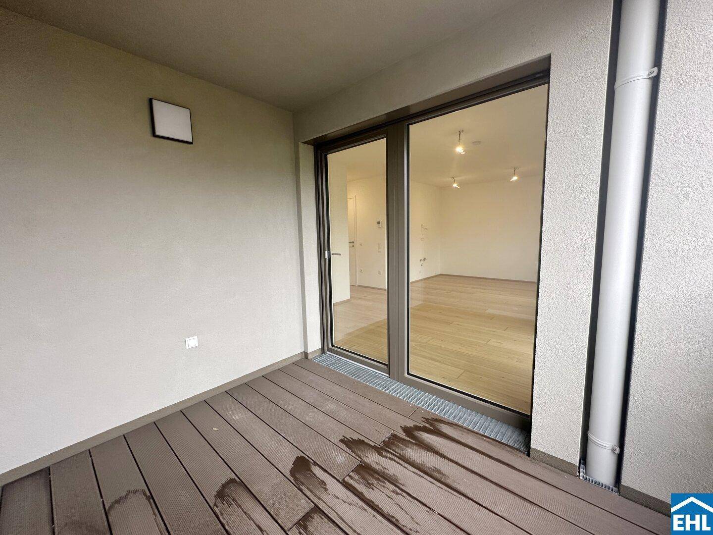 Überdachter Balkon mit Holzdielen und großen Schiebetüren, die zum Innenraum führen.