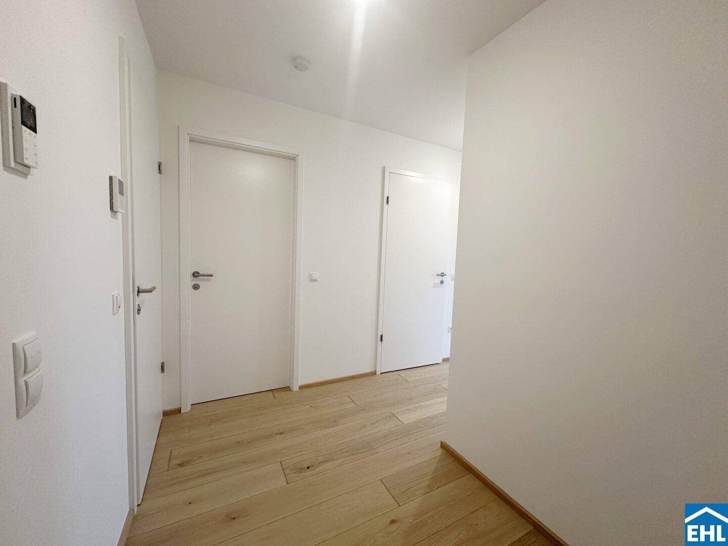 Heller Flur mit mehreren weißen Türen und durchgehendem Parkettboden.