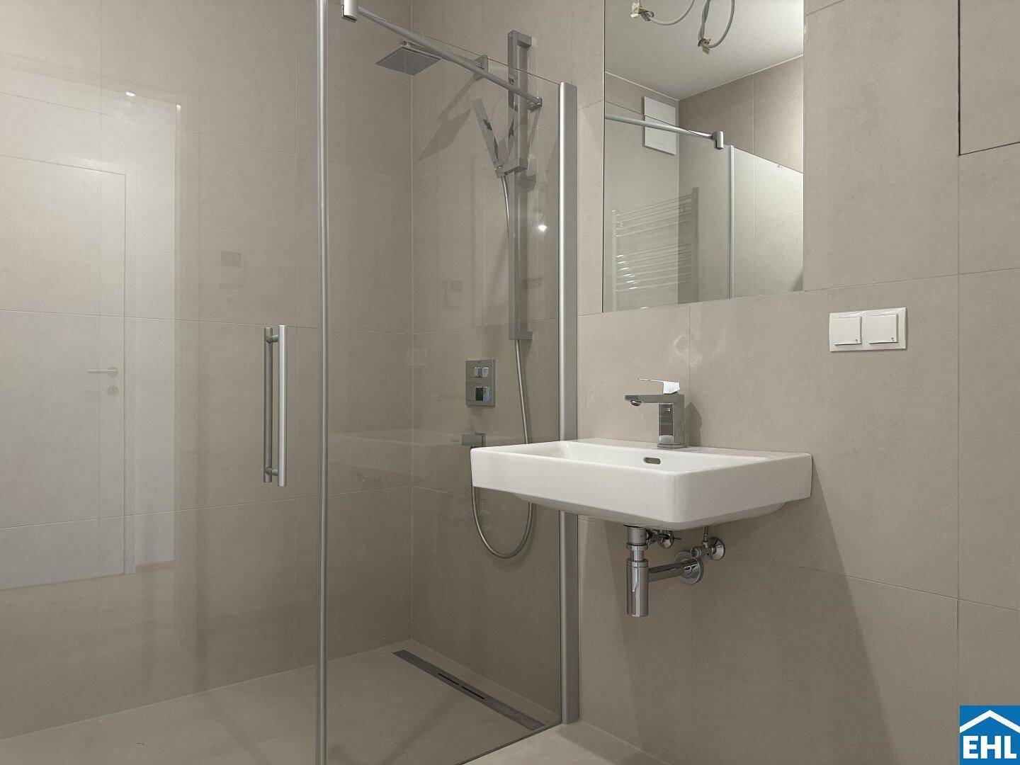 Modernes Badezimmer mit begehbarer Dusche, Wandwaschbecken und hellen, großformatigen Fliesen.