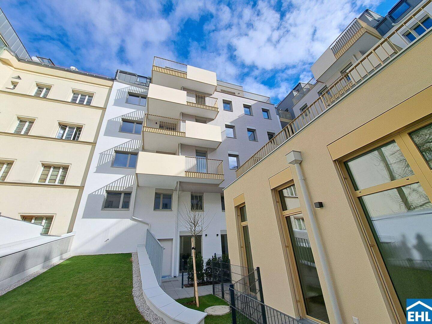 Moderne Wohnanlage mit gepflegter Grünfläche im Innenhof und Balkonen unter blauem Himmel.