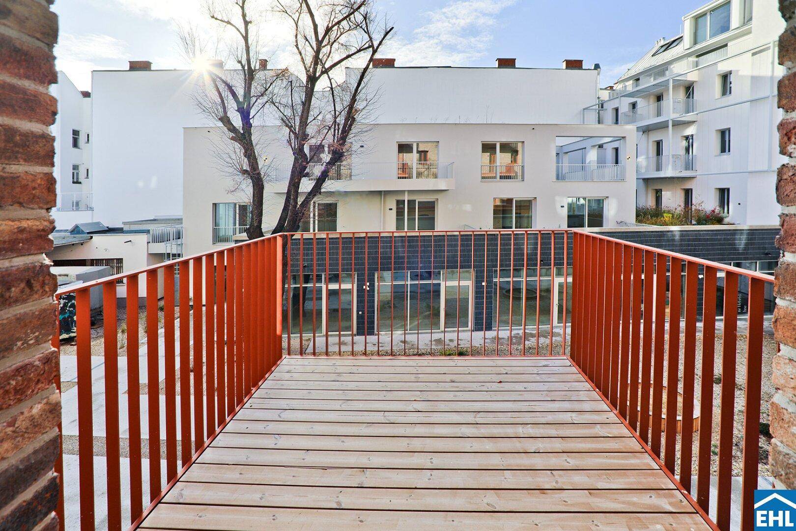 Geräumiger Balkon mit Holzbelag und Blick auf den Innenhof und moderne Gebäude.