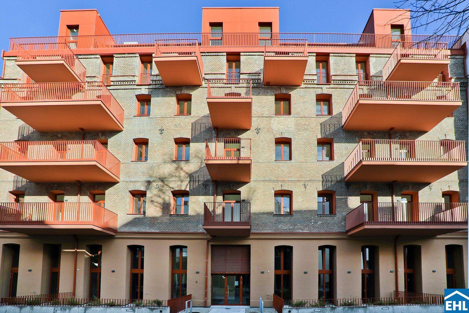 Fassade eines modernen Wohngebäudes mit markanten orangefarbenen Balkonen und Ziegelmauerwerk.