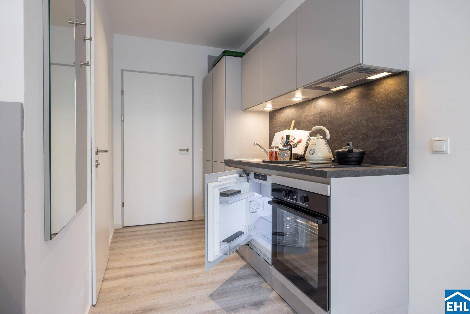 Kompakte Küchenzeile in einem Studio-Apartment mit integriertem Kühlschrank und Backofen.