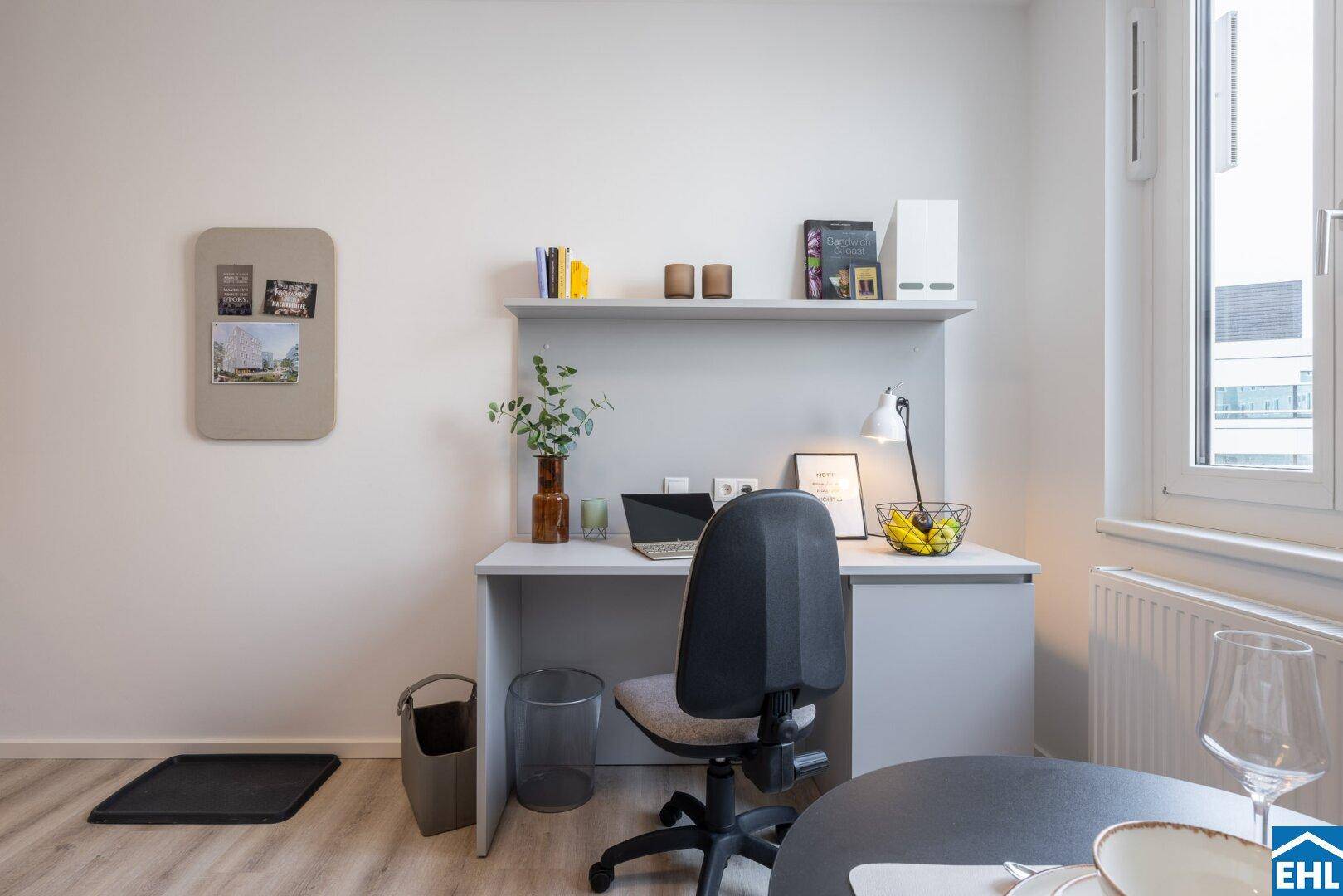 Heller Arbeitsbereich in einem Studio-Apartment mit Schreibtisch und Regal.
