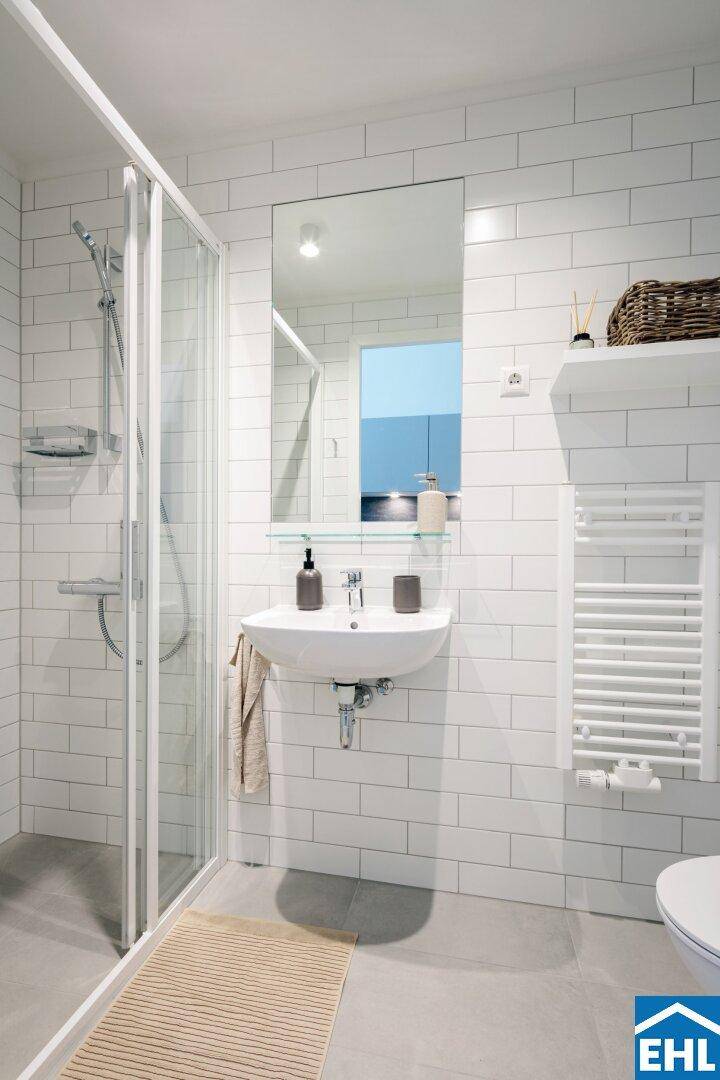 Modernes Badezimmer mit weißen Fliesen, Dusche und beheiztem Handtuchhalter.
