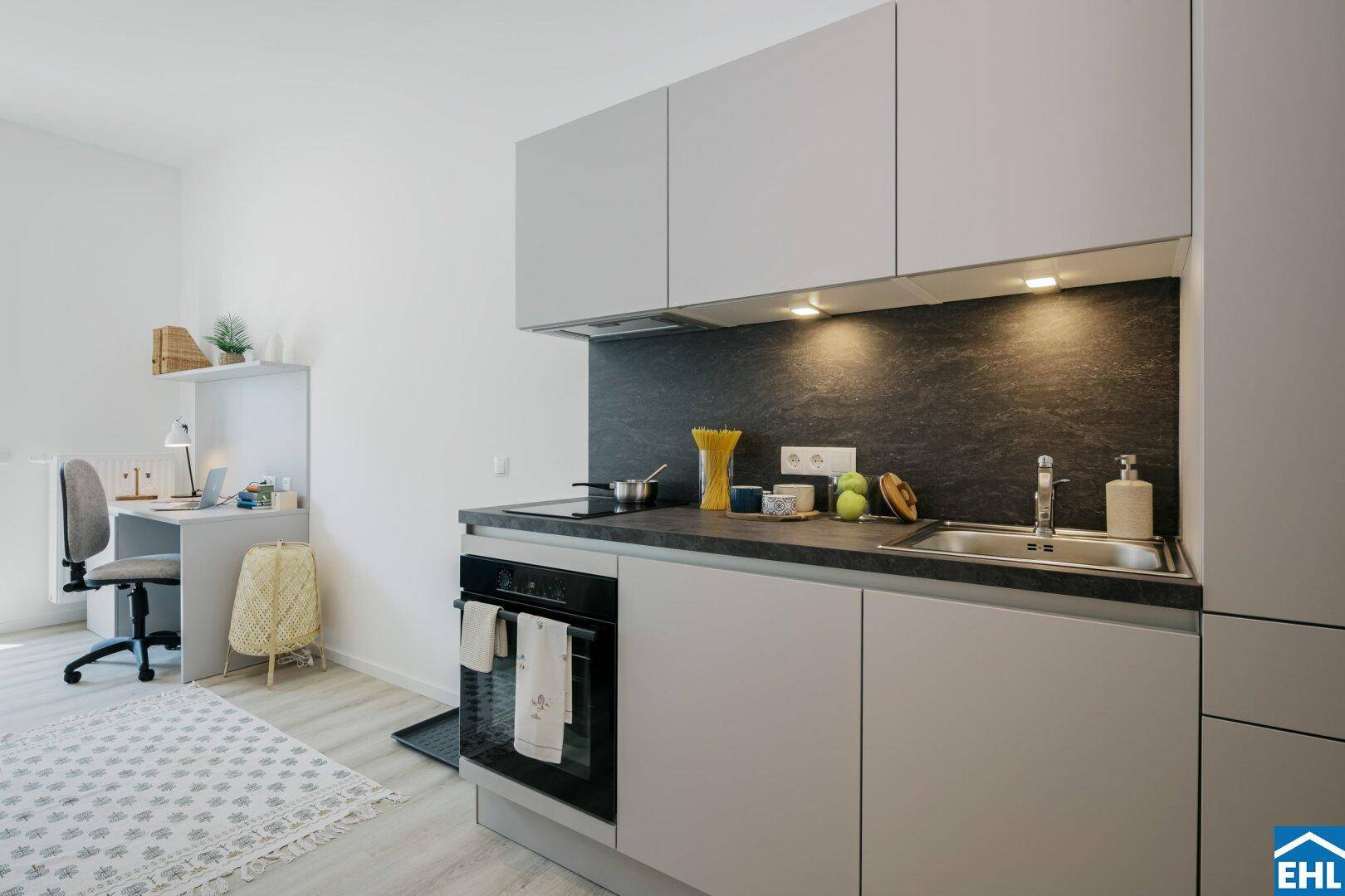 Moderne Küchenzeile im Studio-Apartment mit dunkler Arbeitsplatte und integrierten Geräten.