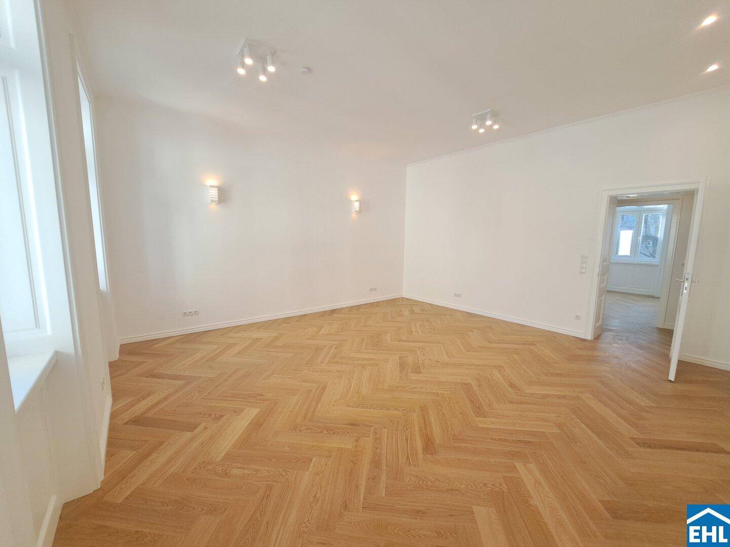 Heller Wohnbereich mit elegantem Fischgrätparkett und modernen Wandleuchten, frisch renoviert.