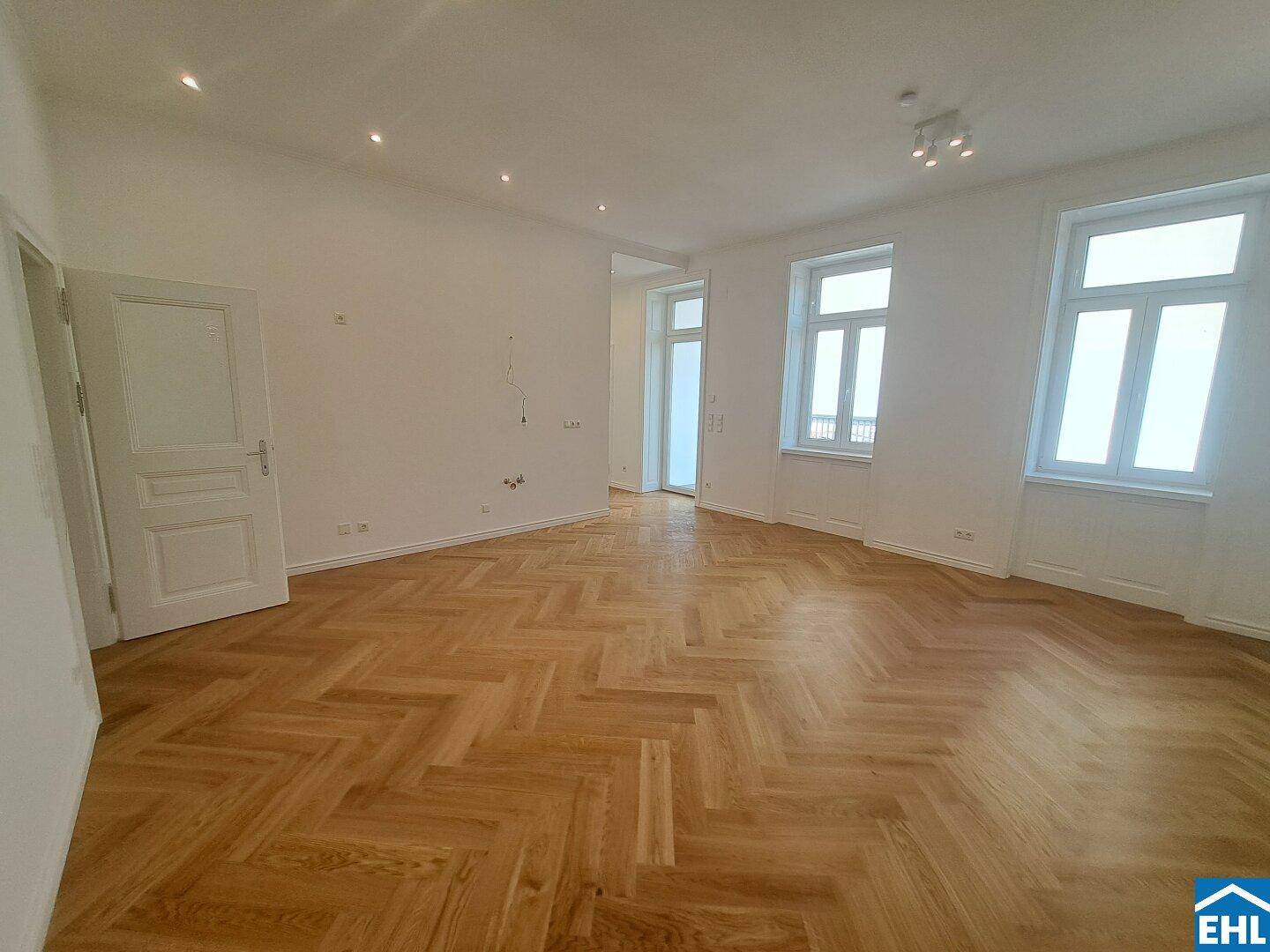 Geräumiges, helles Wohnzimmer mit Fischgrätparkett und hohen Fenstern, bereit für die Einrichtung.