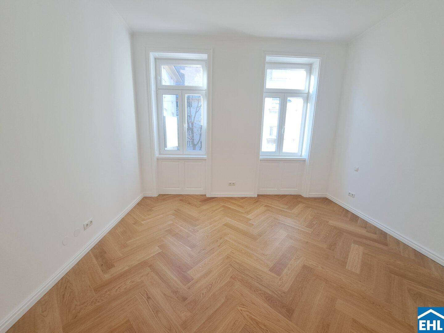 Helles Schlafzimmer mit klassischem Fischgrätparkett und zwei hohen Fenstern.