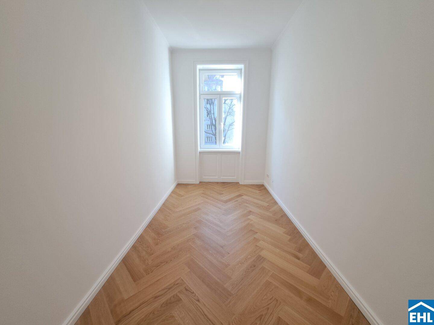Schmaler, heller Raum mit Fischgrätparkett und einem hohen Fenster, ideal als Kinderzimmer.