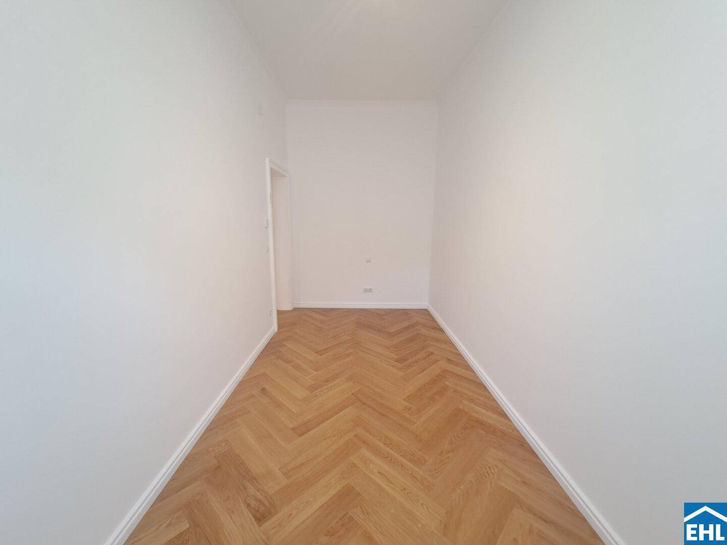 Leerer Raum mit Fischgrätparkett und weißen Wänden, vielseitig nutzbar.