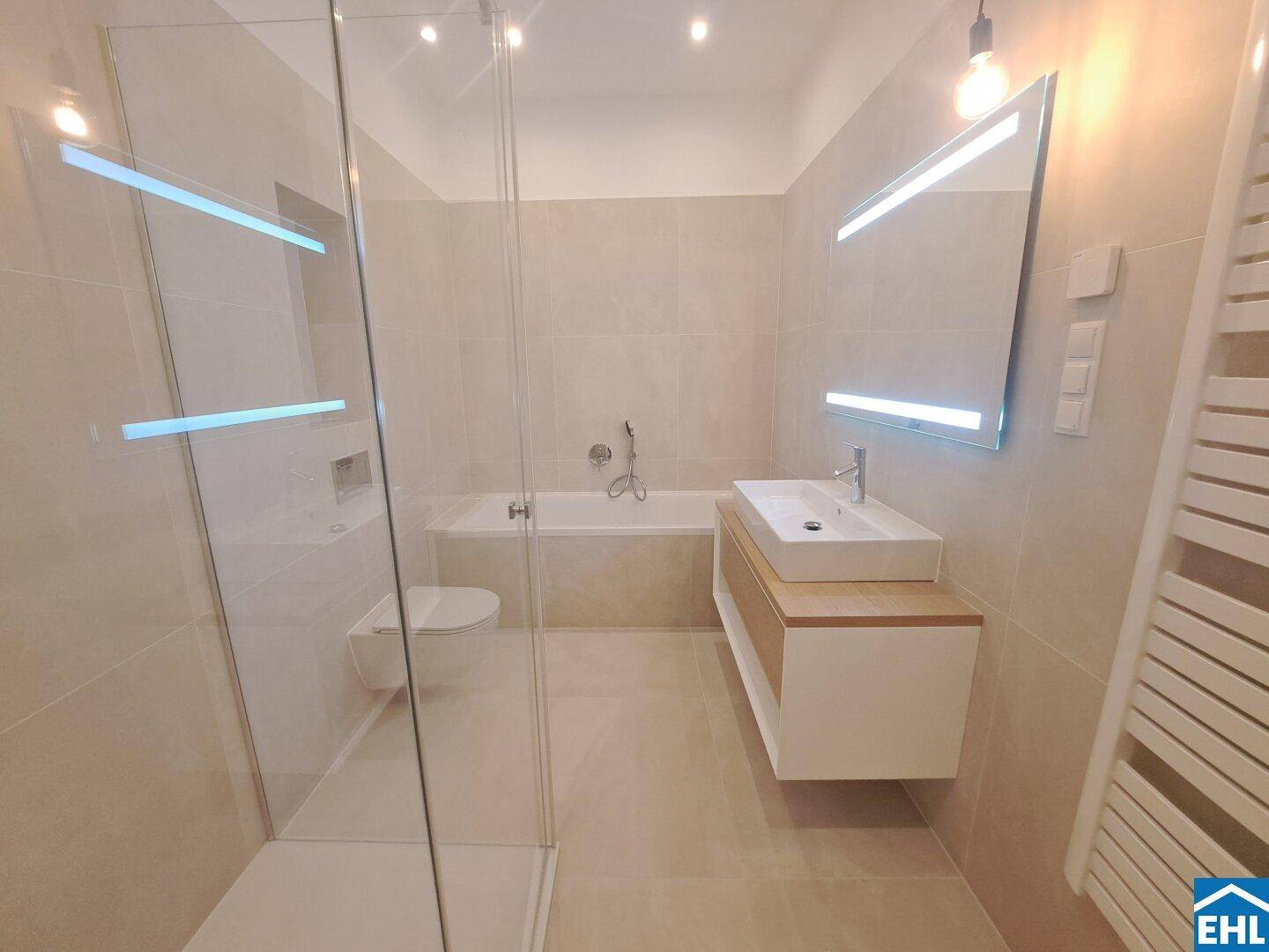 Modernes Badezimmer mit begehbarer Dusche, Badewanne und beleuchtetem Spiegel.