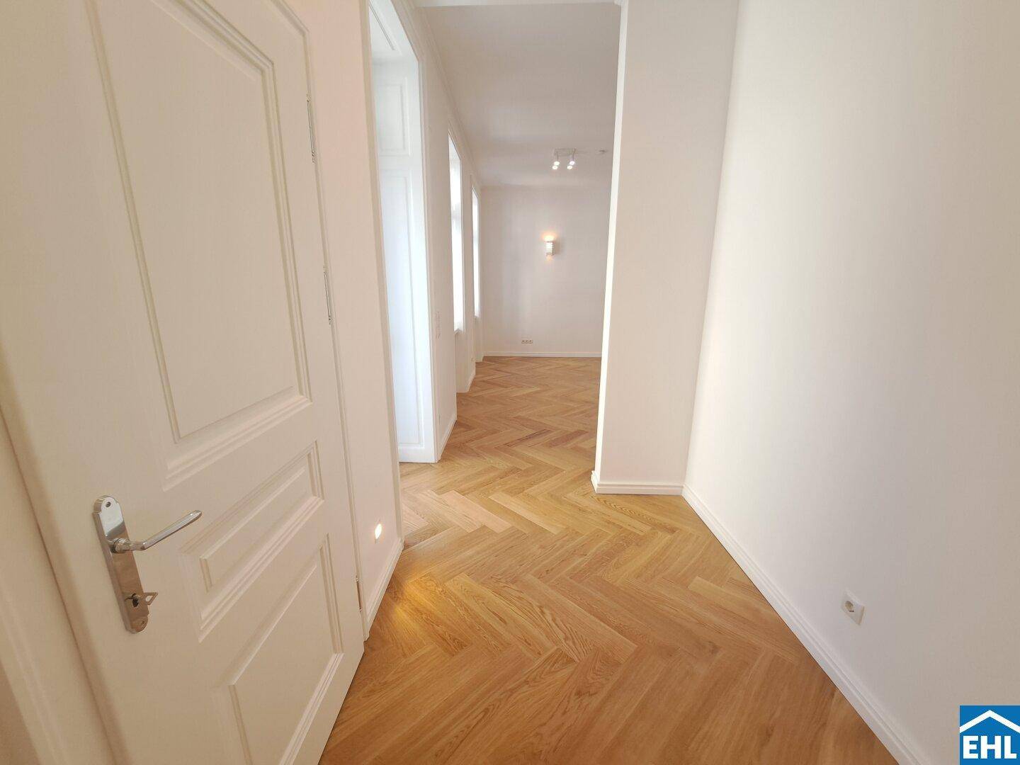Heller Flur mit Fischgrätparkett und weißen Türen, verbindet die verschiedenen Räume.