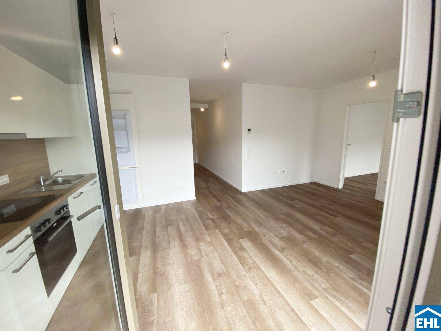 Blick vom Wohnbereich in den Flur, mit offener Küche und modernem Laminatboden.