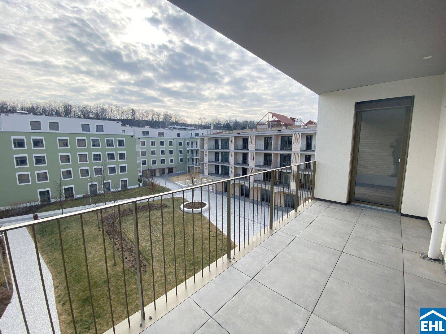 Geräumiger Balkon mit Fliesenboden und Blick auf den begrünten Innenhof.