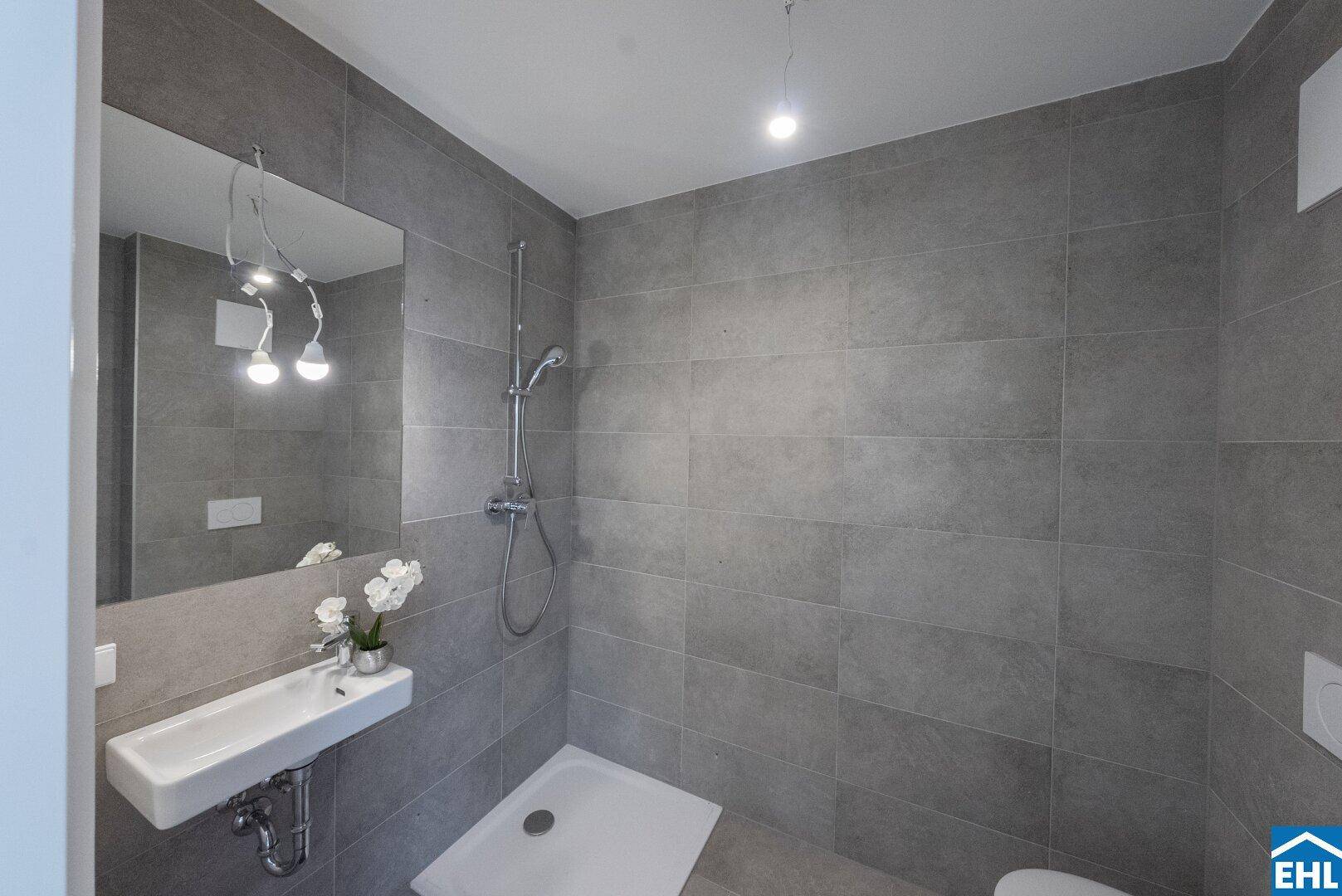 Modernes Badezimmer mit grauen Fliesen, Dusche und kleinem Waschbecken.