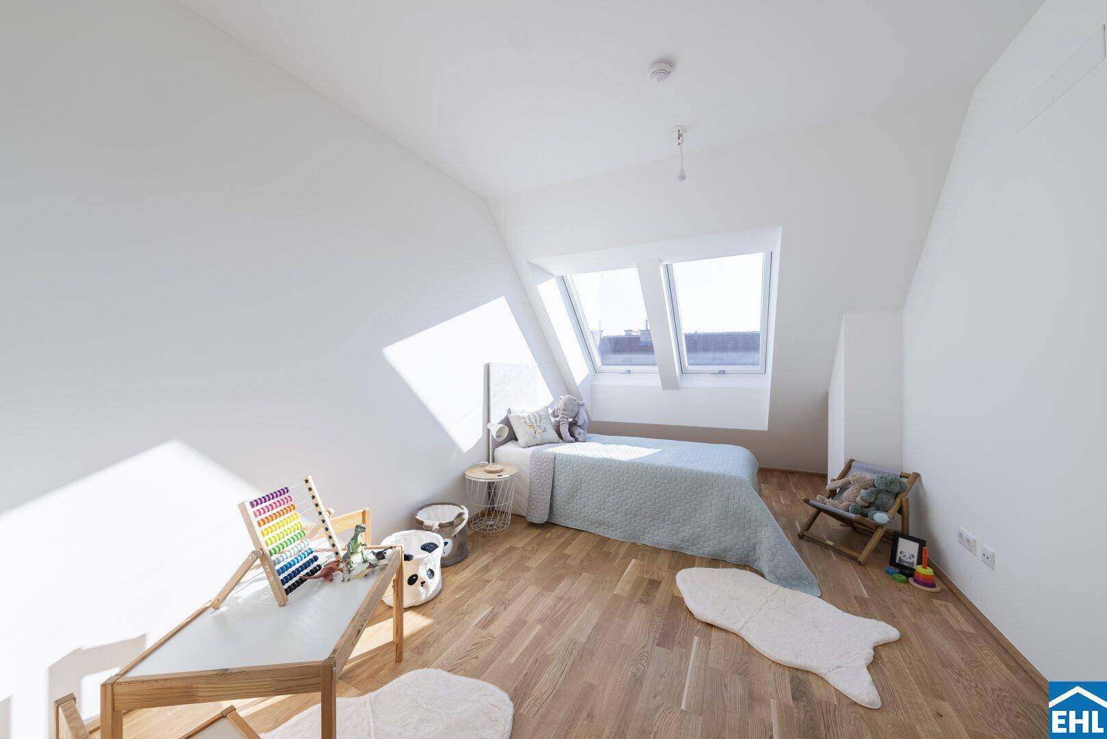 Kinderzimmer mit Holzboden, Spielzeug und viel Tageslicht durch die großen Dachfenster.