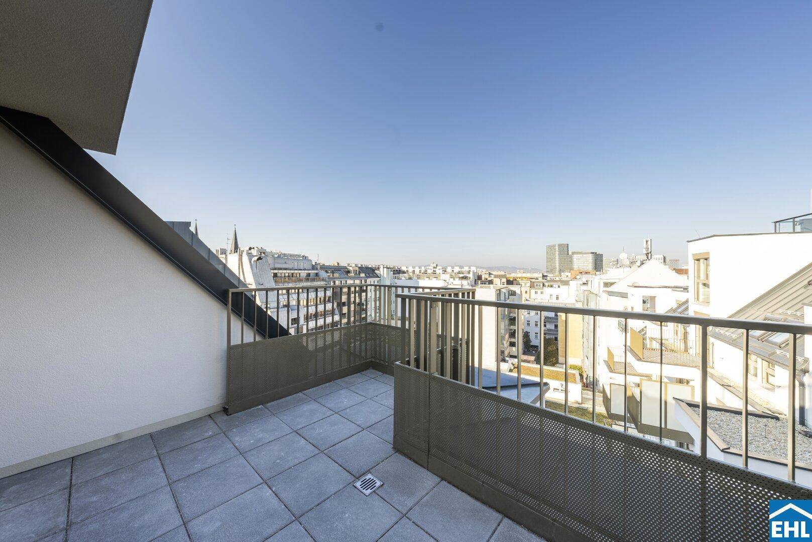 Sonnige Dachterrasse mit Panoramablick auf die Stadt und umliegende Gebäude unter blauem Himmel.