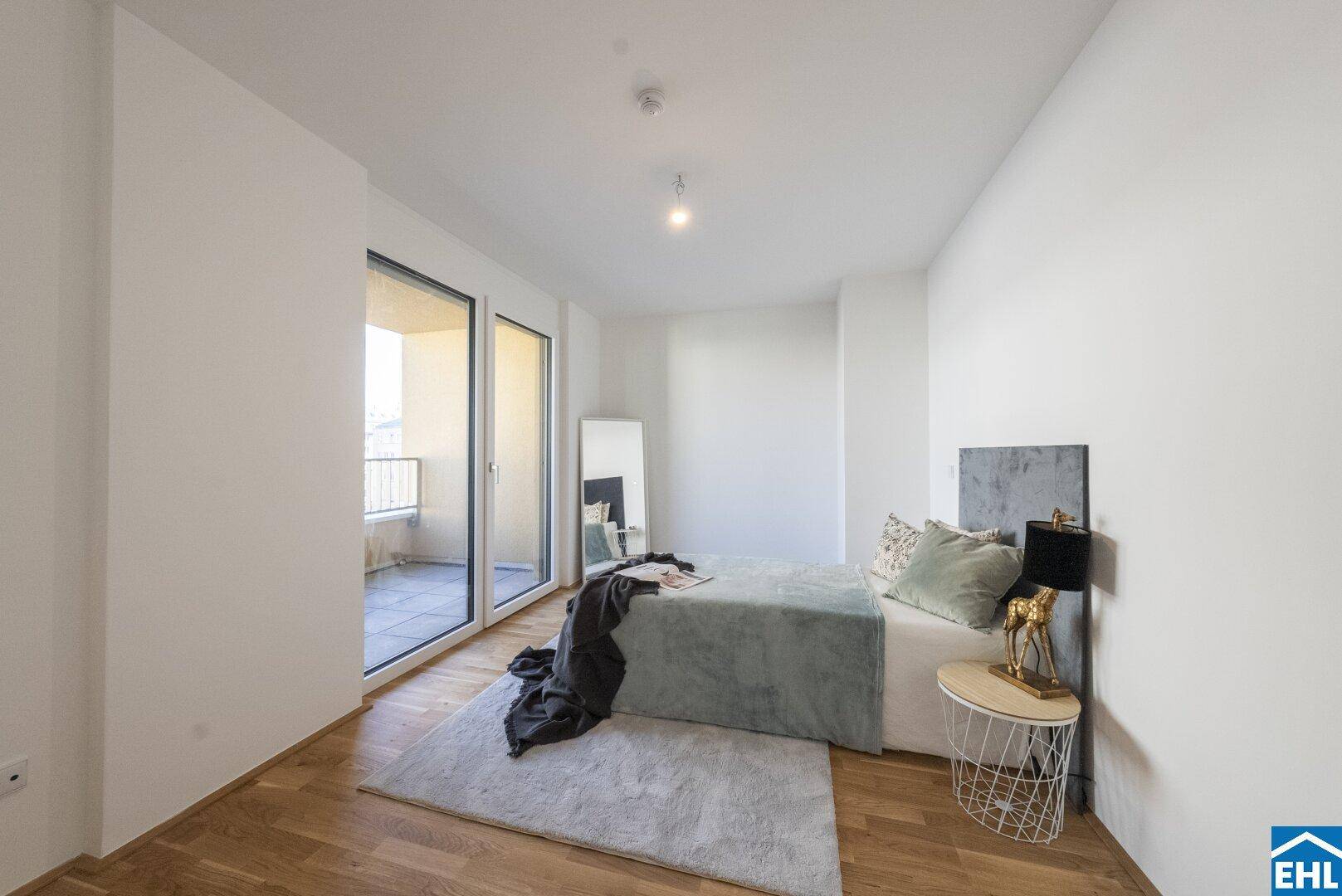 Helles Schlafzimmer mit Holzboden, modernem Bett und Zugang zu einem Balkon.